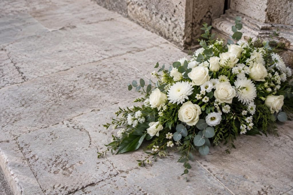 Rouwstuk van witte rozen en groen op een oude stenen ondergrond
